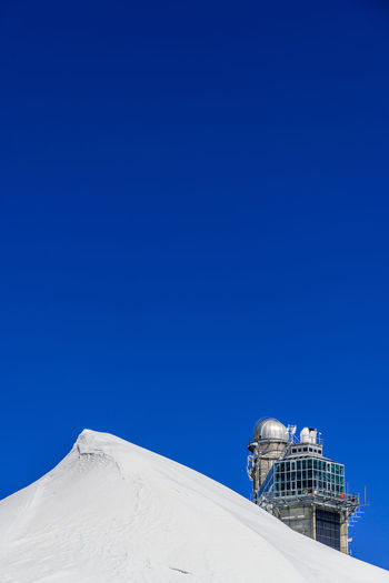 Low angle view of sphinx observatory on snowcapped mountain against clear blue sky