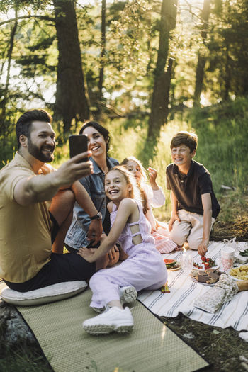 Father taking selfie with family through smart phone during picnic
