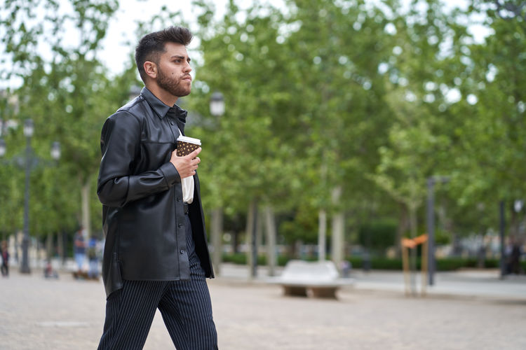 Young man holding reusable cup while walking in city