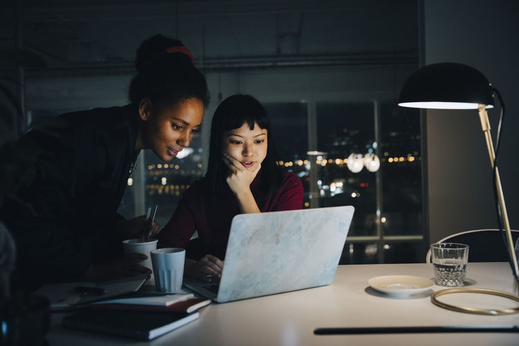 Confident businesswomen planning strategy while using laptop in night meeting at office