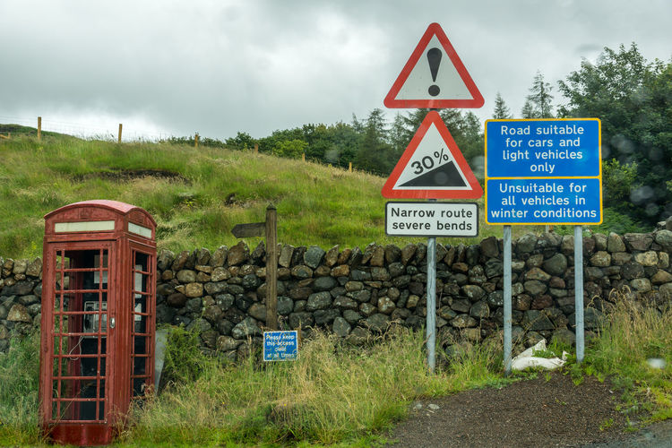 Old telephone booth and road signs on hardknott pass against cloudy sky
