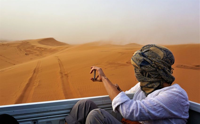 Man sitting in vehicle at desert against sky