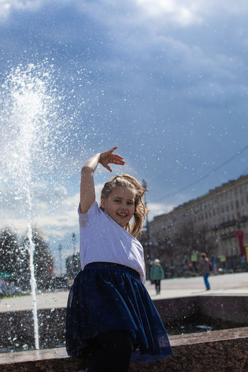 Happy little cute girl having fun in splashes a fountain