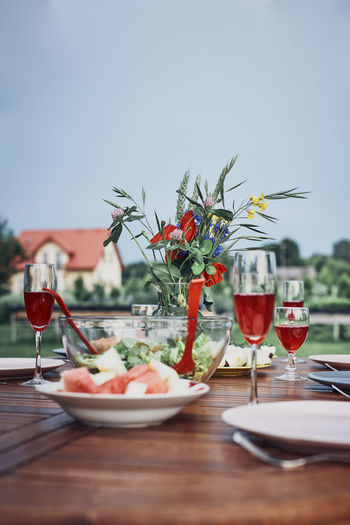 Dinner in an apple orchard garden on wooden table with salads and wine decorated with flowers