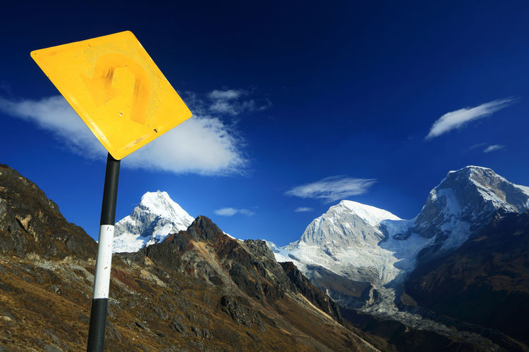 Low angle view of yellow signpost by mountain peaks against blue sky