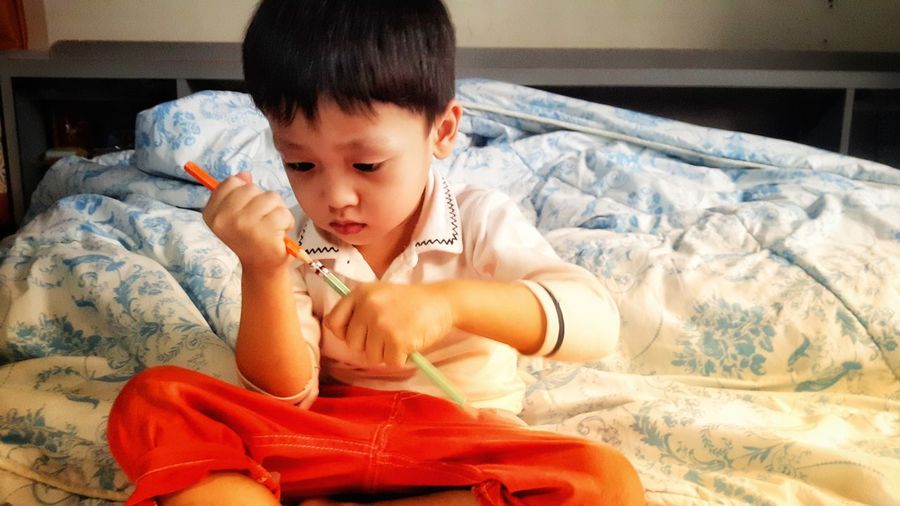 Cute baby boy sitting on bed at home