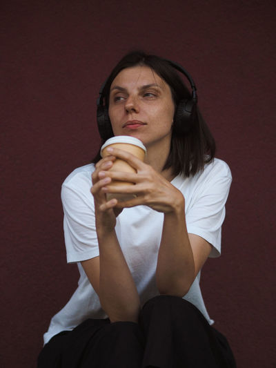 Thoughtful young woman with headphones listening to music and drinking coffee.