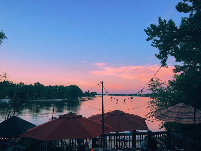 People at huts at riverbank during sunset