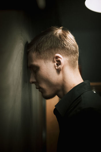 Side view of thoughtful young man standing leaning on wall