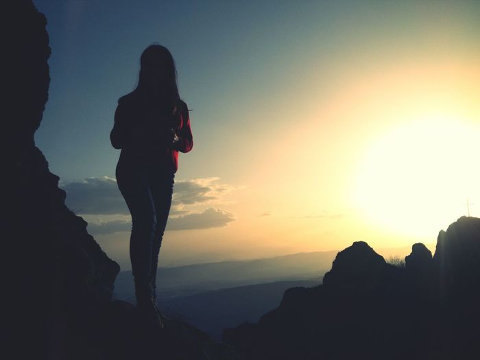 Woman standing on cliff against sky during sunset