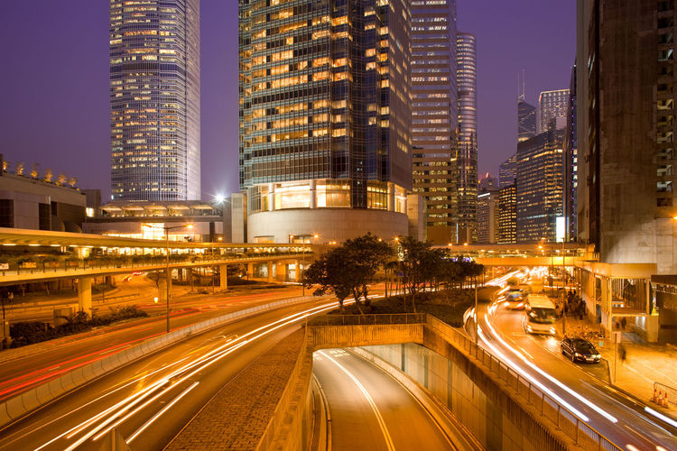 Light trails on road by illuminated buildings in city at dusk