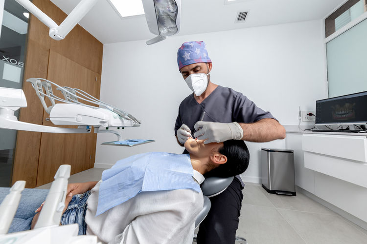 Male dentist with uniform standing while examining the mouth of a female patient in a dental clinic