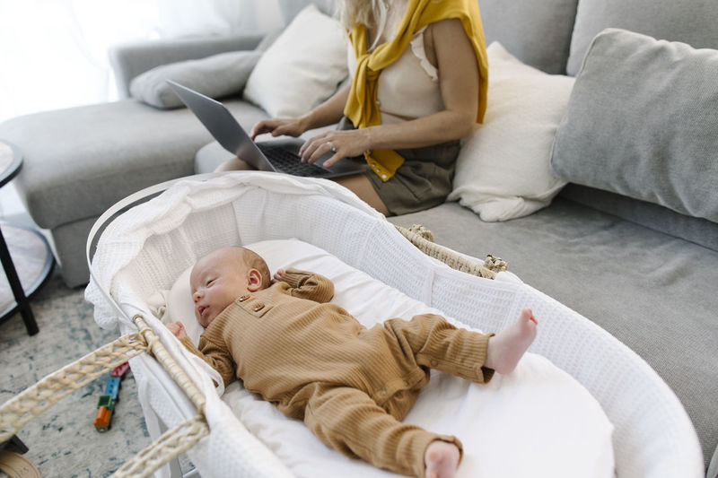 Woman using laptop sitting by baby sleeping in crib at home