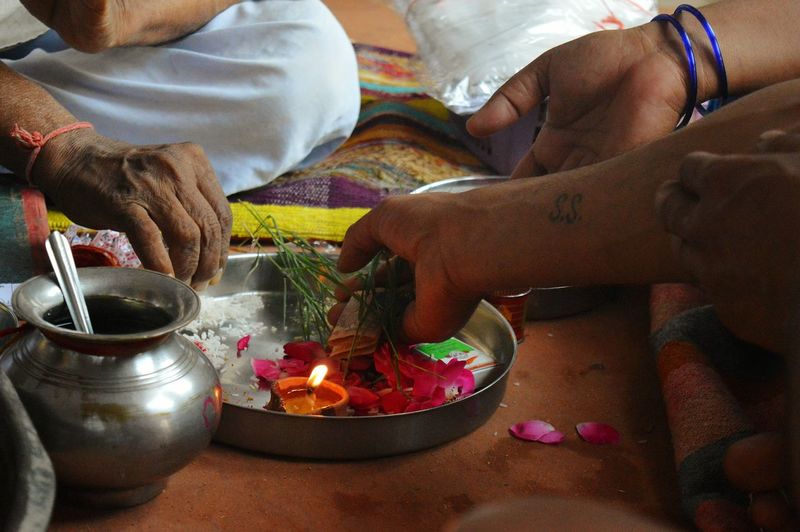 Cropped hands of people keeping religious offerings and paper currency in plate