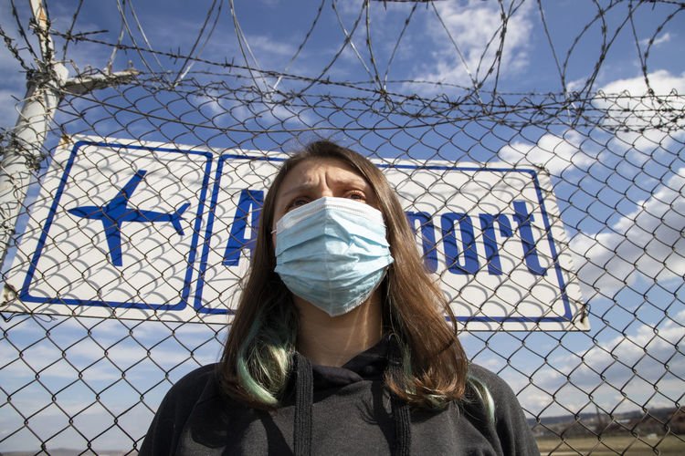 Low angle view of woman wearing mask standing against fence
