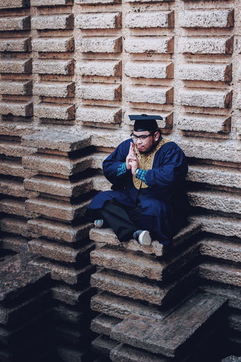 Man wearing mortar board sitting at build structure