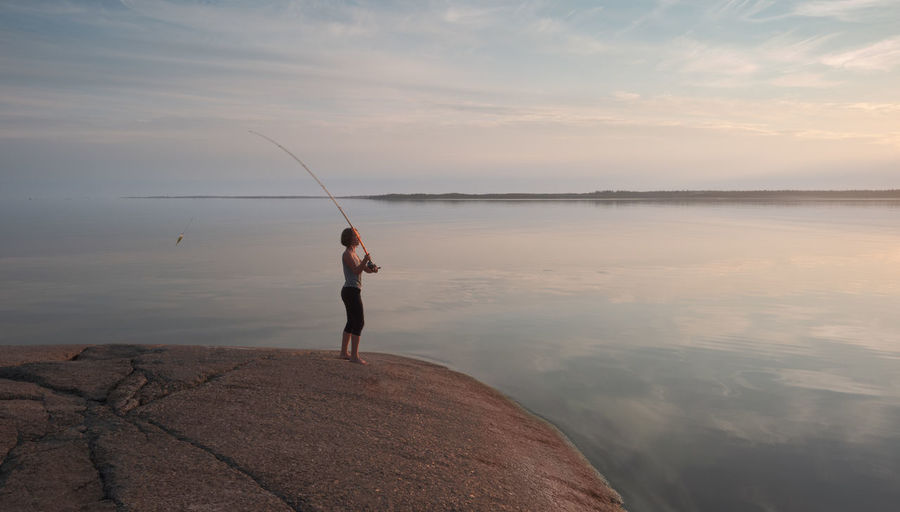 The fisherwoman throws a bait. girl with a fishing rod on a granite shore in a picturesque place.