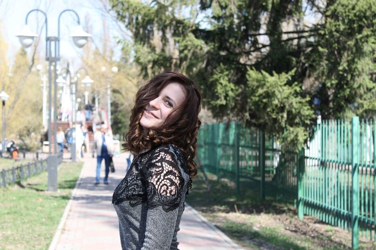 Portrait of smiling young woman standing on footpath