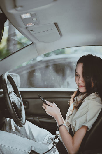 Cinematic style young women on driver position and hand holding smart phone , car interior