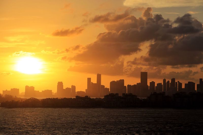 Sea by cityscape against sky during sunset