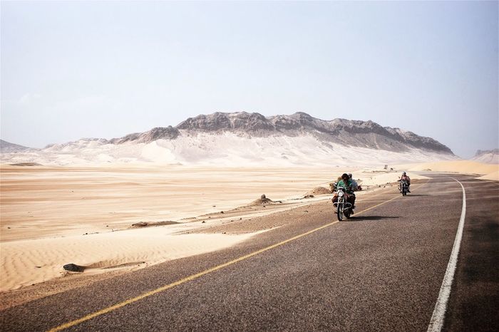 REAR VIEW OF PEOPLE RIDING BICYCLE ON DESERT