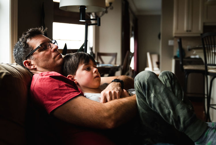 Father holding his son on his lap while sitting on a couch at home.