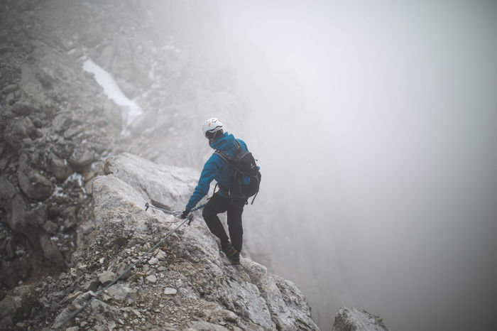 Full length rear view of hiker walking on rocky mountain during foggy weather