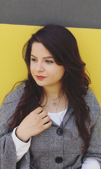 Portrait of beautiful young woman standing against yellow wall