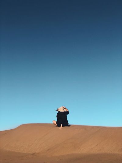 Rear view of woman siting at desert against clear blue sky