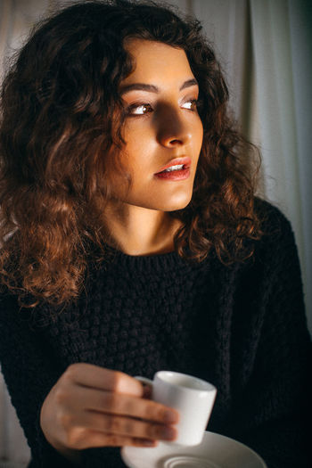 Thoughtful woman with cup looking away at home