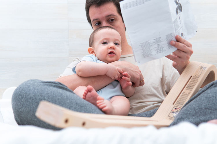 Father reading book while sitting with baby at home