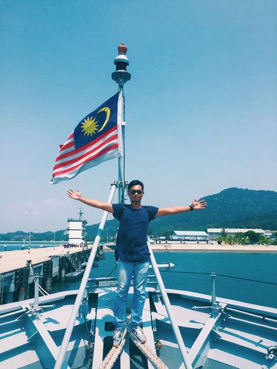 Man with arms outstretched by malaysian flag in boat at sea