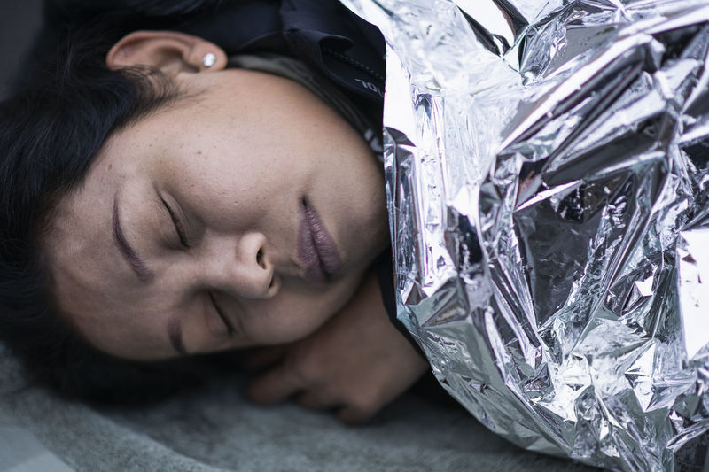 Unconscious woman in medical shock lying under emergency blanket