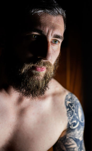 Close-up of shirtless man looking away in darkroom