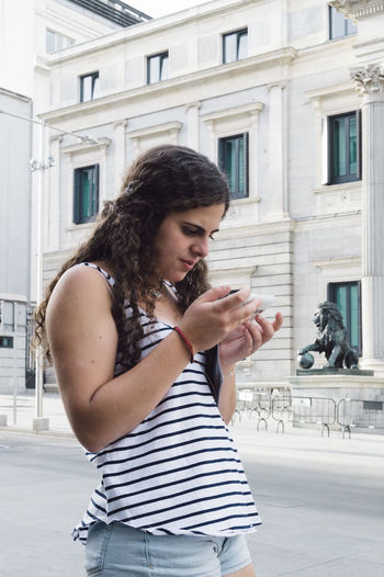 Young woman using mobile phone while standing against buildings