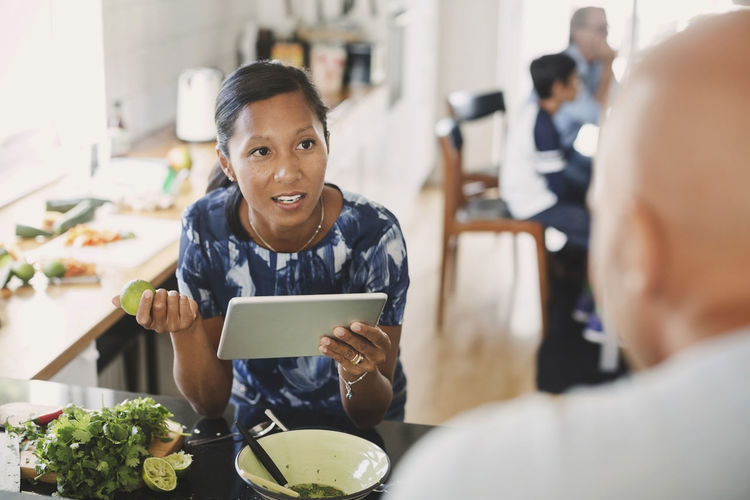 Woman talking to man while holding digital tablet in kitchen