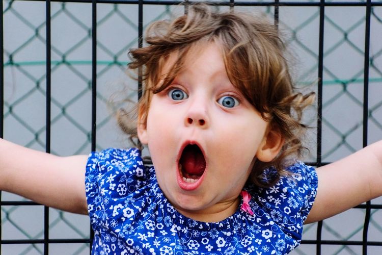 Close-up of shocked girl with mouth open against fence