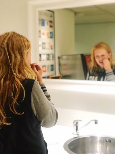 Rear view of girl brushing teeth while standing in bathroom