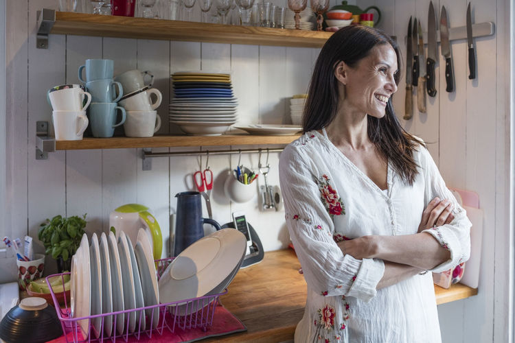 Happy woman standing by counter with arms crossed in kitchen at home