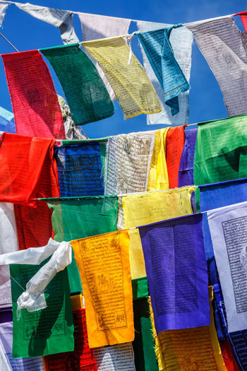 Close-up of multi colored flags hanging against blue sky