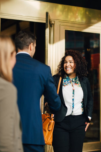 Smiling businesswoman greeting mature businessman by female colleague standing against building