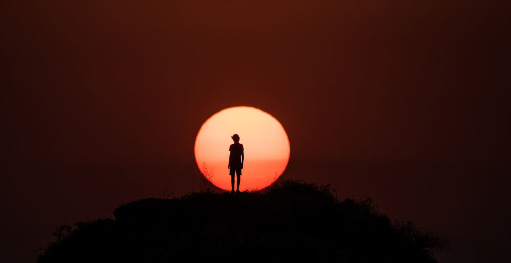 SILHOUETTE MAN STANDING AGAINST ORANGE SUN