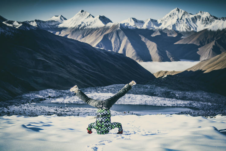 Young man doing headstand against mountains on snow
