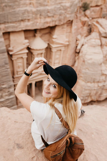 Portrait of young woman in hat sitting on rock formation