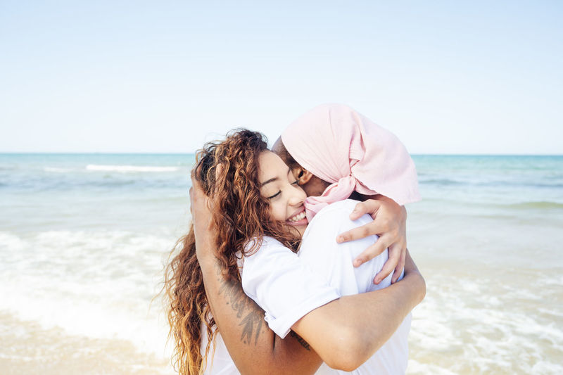Side view of content african american adult mother and young daughter standing on beach near sea