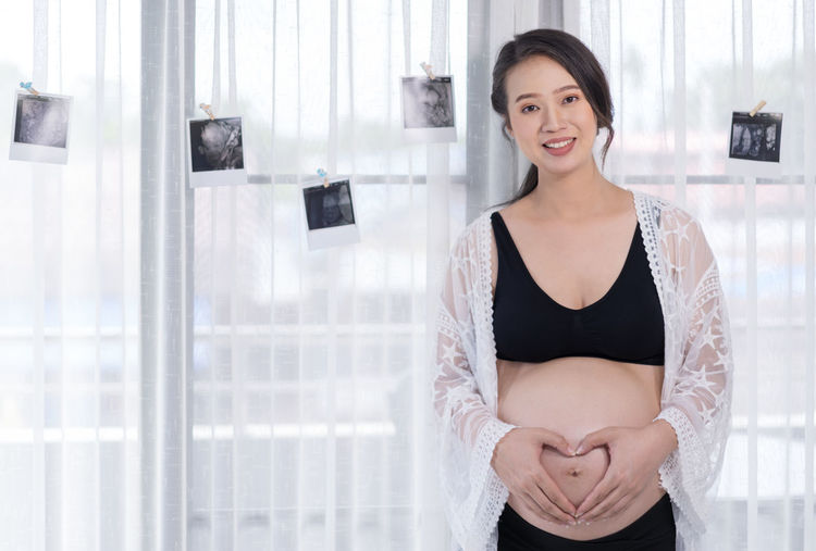 Portrait of smiling pregnant woman standing at home