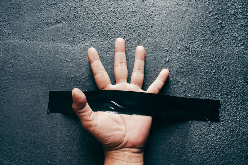 Cropped hand of person with adhesive tape on wall