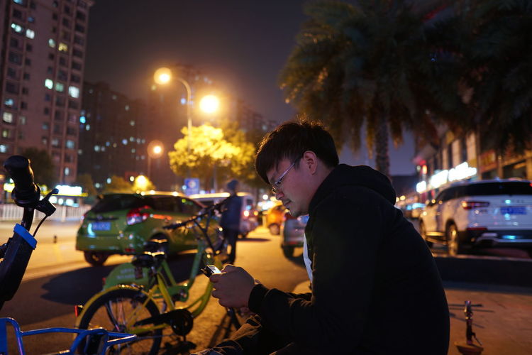Side view of man using phone on street at night