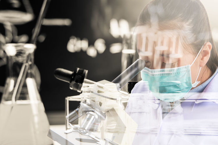 Double exposure of female doctor looking in microscope in laboratory