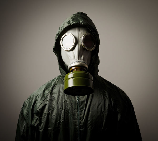 Portrait of person wearing gas mask while standing against gray background